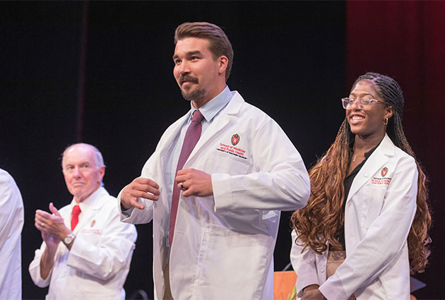 Medical student Mike Plaza receiving his first white coat from faculty