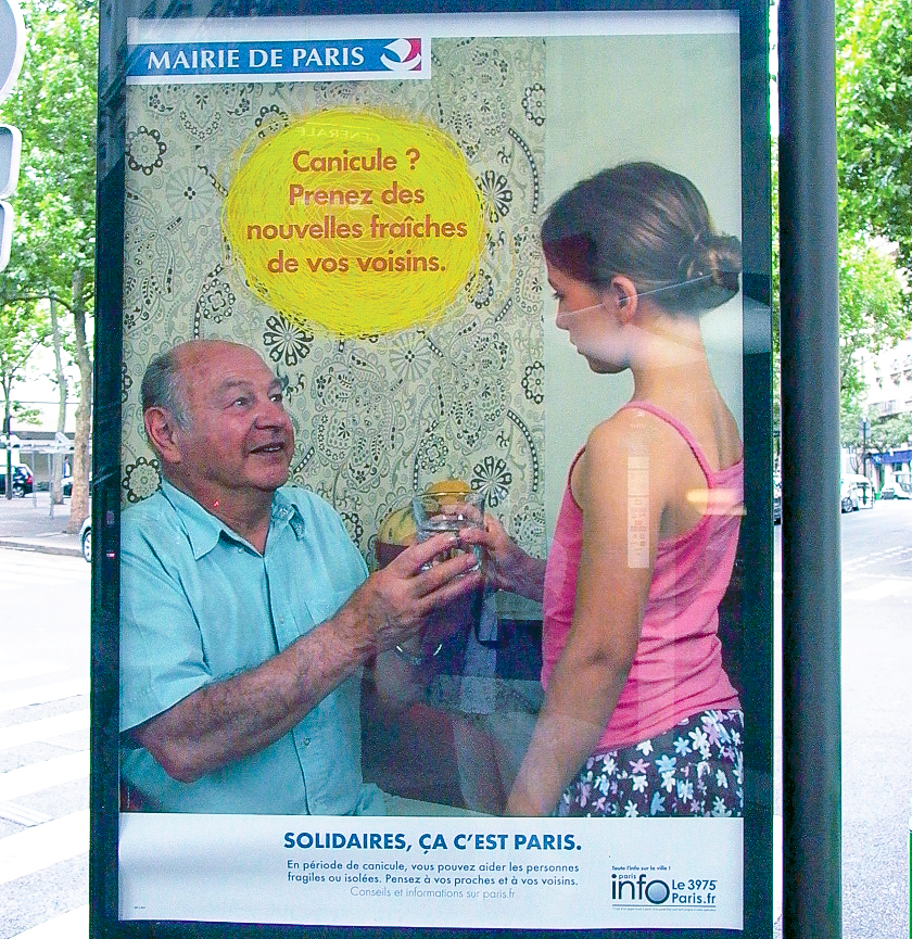 A street-level billboard shows a girl handing an older neighbor a glass of water.