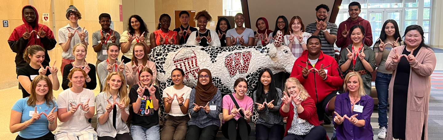 A group RUSCH students smiling in front of a mosaic-covered cow sculpture in the HSLC atrium