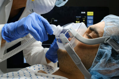 The gloved hand of a hospital employee adjusts a patient's ventilation mask