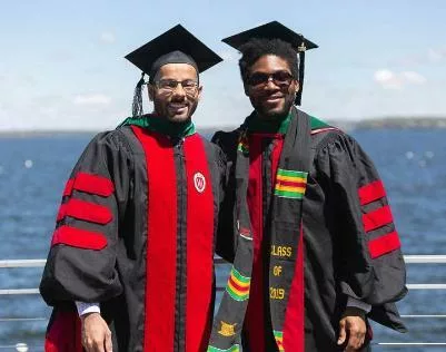 Two students in graduation gowns posing lakeside