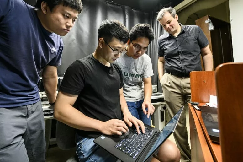 Three students and a professor huddled around a laptop computer